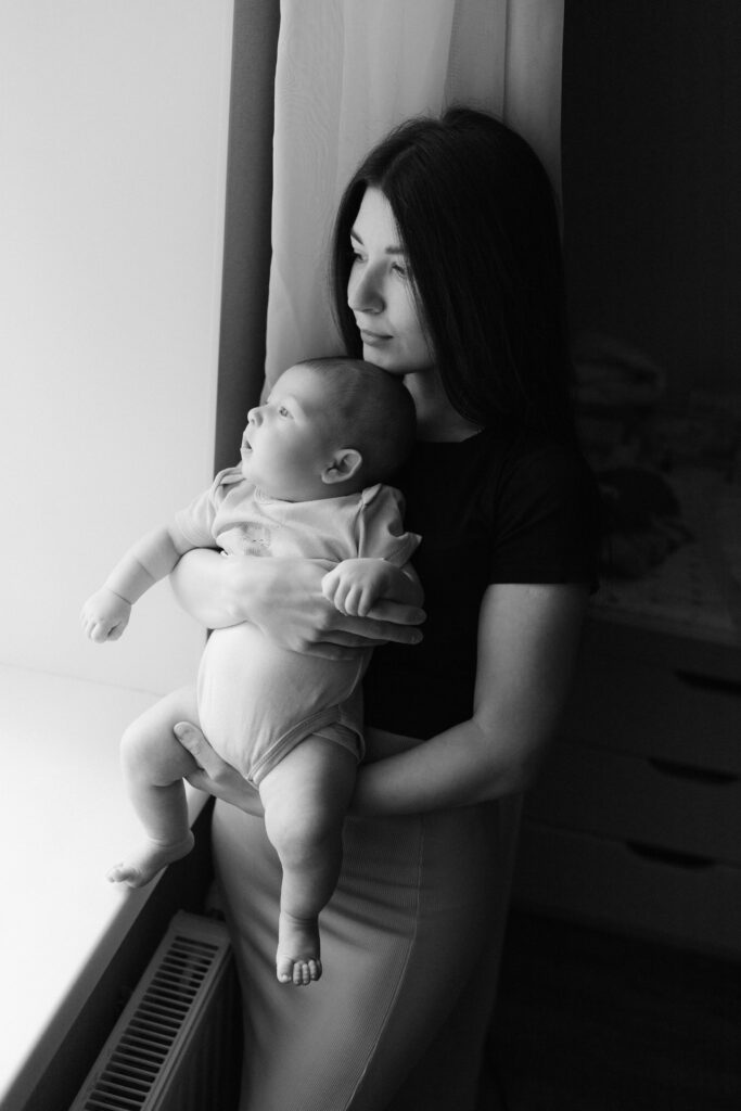 An image of a woman sitting by a winder holding her baby. What to expect in the Postpartum period.